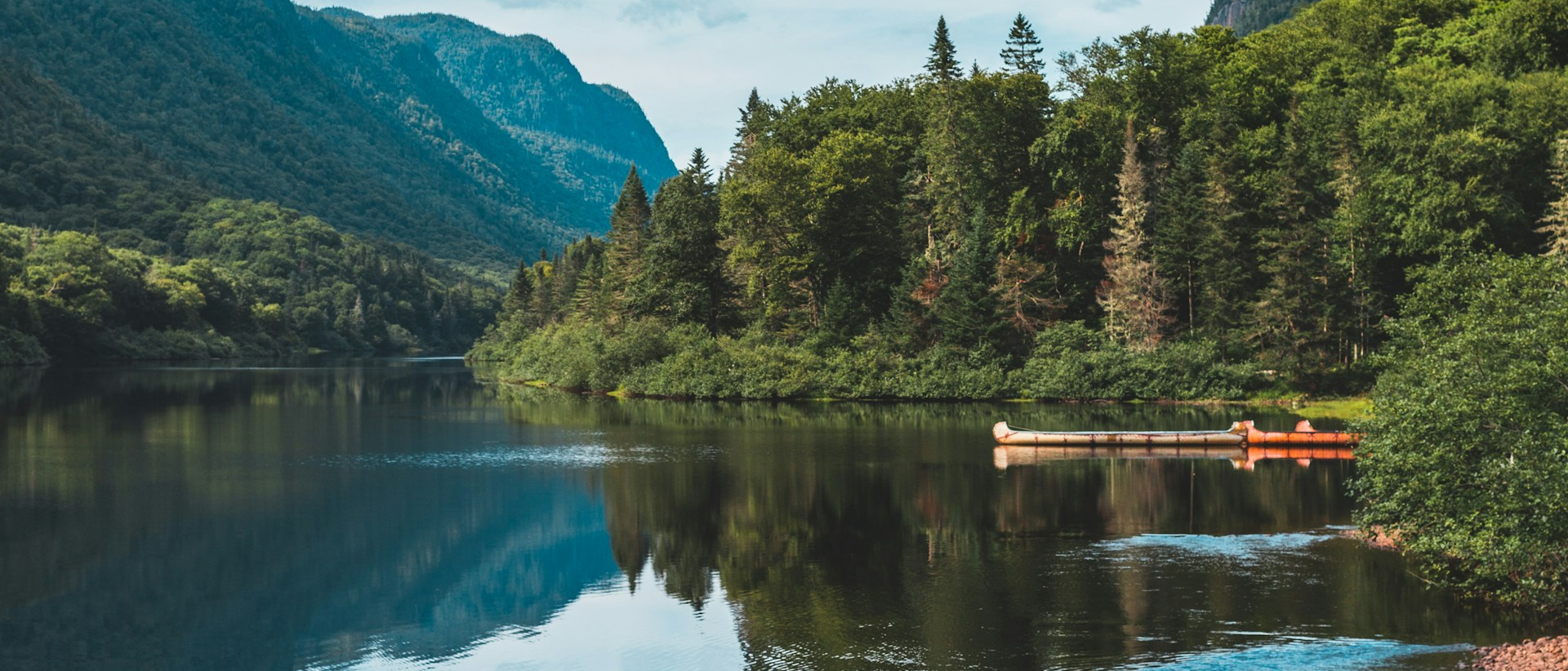 A picture of a lake surrounded by trees, with an orange kayak visible on the right side. Photo by Alice Triquet on Unsplash.